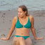 Kvinde siddende på strand i flot grøn bikini